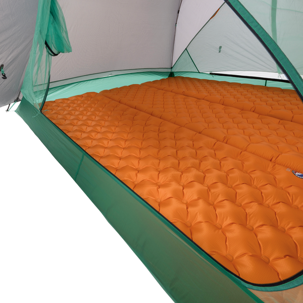An orange inflatable sleeping pad covers the floor of the durable Big Agnes Canada Sarvis VST 3 tent, offering a cushioned sleeping surface inside this green and white shelter.