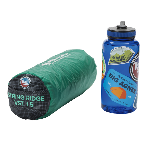 A green, rolled-up Big Agnes String Ridge VST 1.5 ultralight shelter sits next to a blue Nalgene water bottle decorated with outdoor-themed stickers.